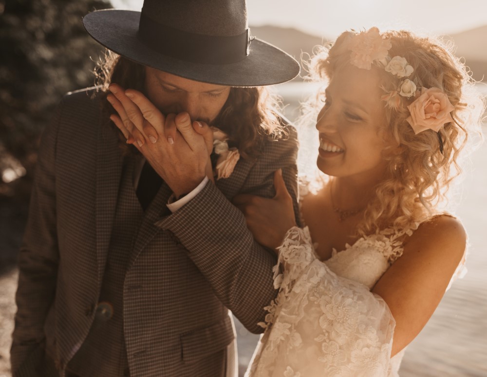 Golden hour bride smiling groom kissing her hand water in the back