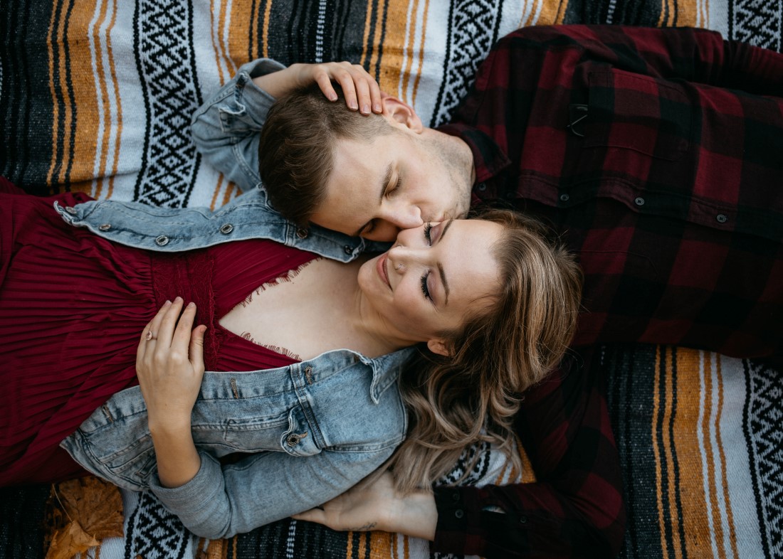 Engaged couple in jean jackets lay on autumn leaves at Hatley Castle