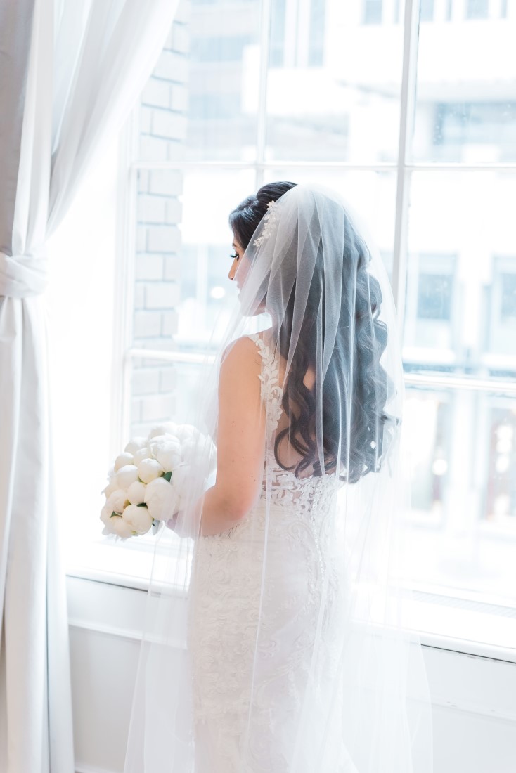 Bridal veil over long curls and holding white rose bouquet by Tala Florist