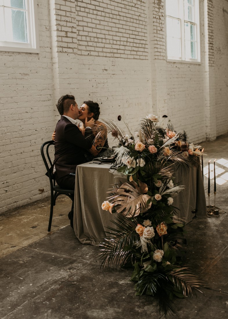 Bride and groom kiss at sweetheart table with floral cascading off the edge