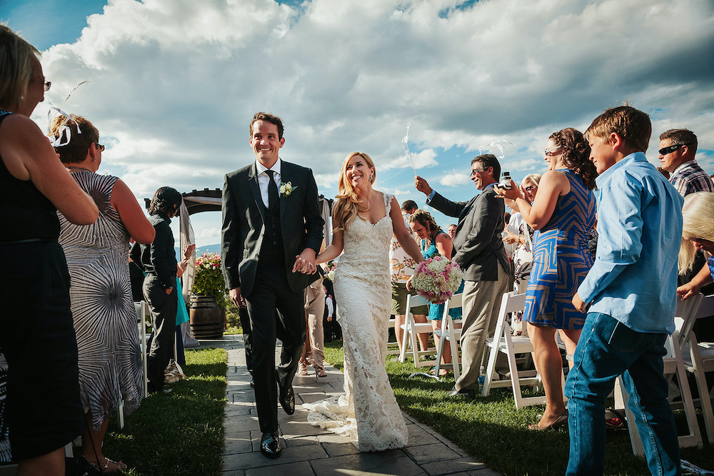 Newlyweds walk up the aisle smiling at guests at Summerhill Winery