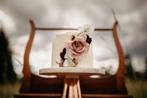 White wedding cake on pedestal in flower meadow by Schur to Please on Vancouver Island