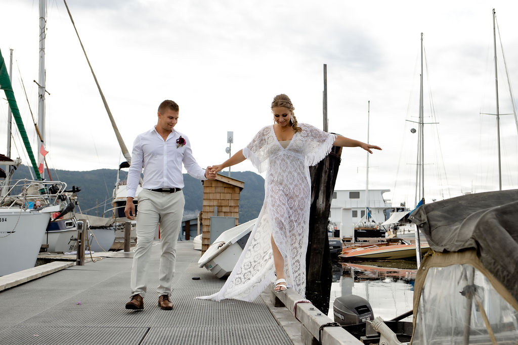 Bride balances along pier as groom holds her hand by Amanda Reed Photos