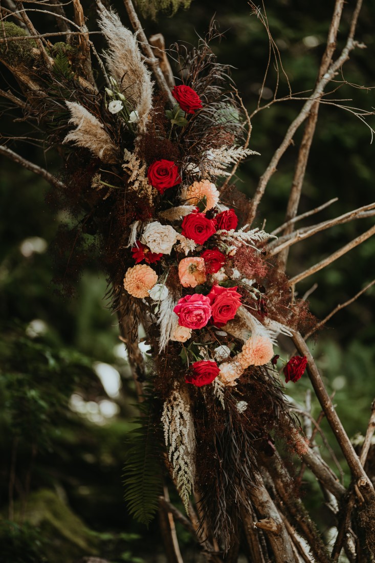 Red and yellow dahlias along a tree branch in a forest wedding