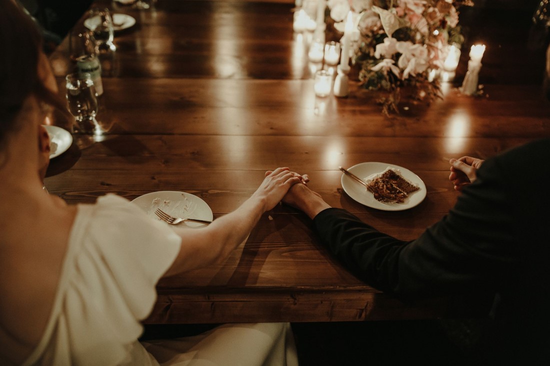 Bride and groom hold hands on reception table in Vancouver backyard