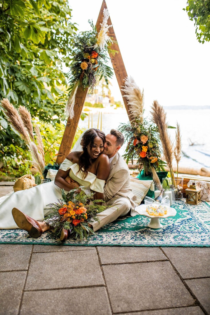 Newlyweds sit in front of triangle arch on Vancouver beach by Bespoke Decor