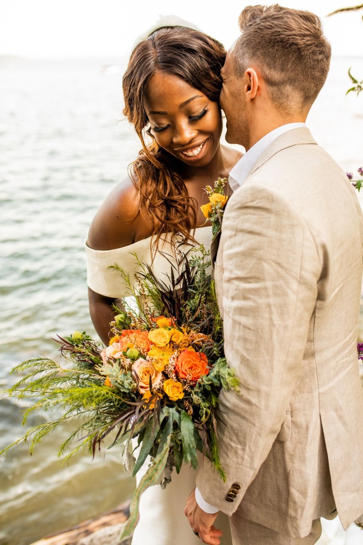 Bride and groom embrace along Vancouver water edge 