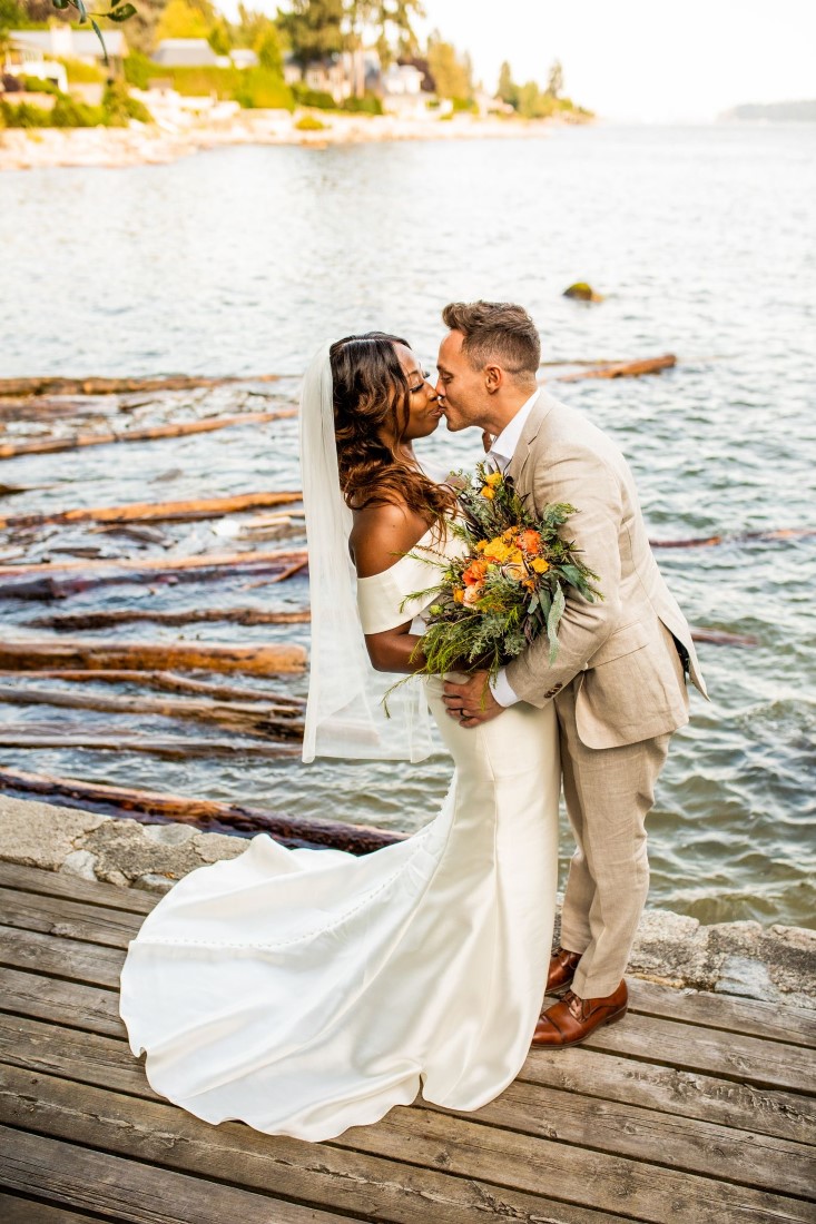 Newlyweds kiss along Vancouver water edge with bride wearing David's Bridal gown and groom in Indochino
