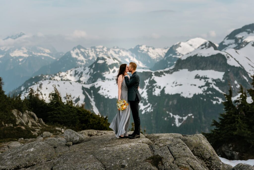 Epic Mountain Views Newlyweds kiss on top of BC Mountains by Leanne Sim Photography
