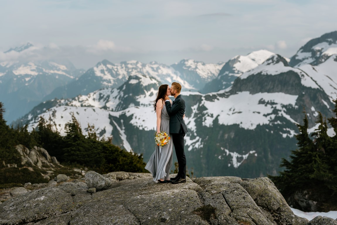 Epic Mountain Views Newlyweds kiss on top of BC Mountains by Leanne Sim Photography