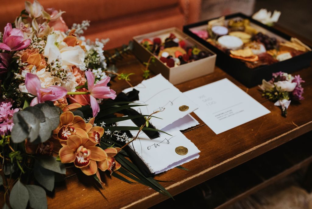 Invitation in Calligraphy sit on a desk with charcuterie boxes by Spoon and Spade