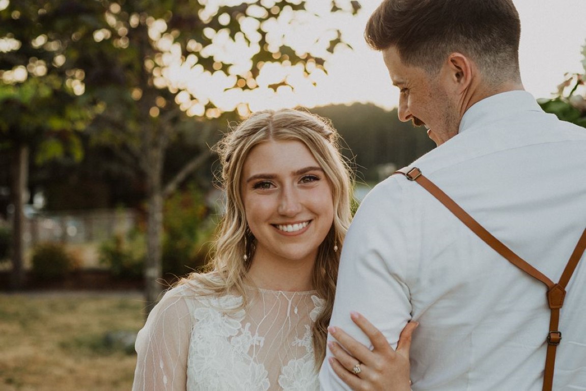 bride smiling at camera holding onto the arm of groom as he gazes down at her