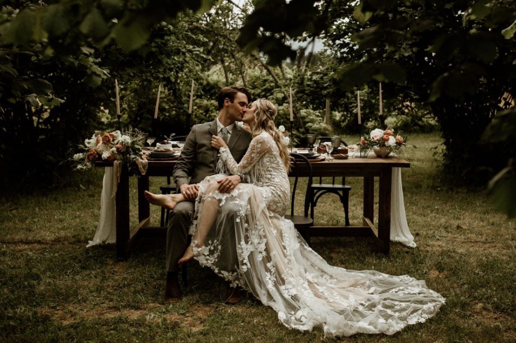 Newlyweds kiss in front of sweetheart table in forest