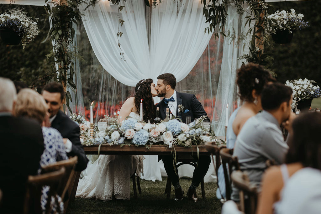 newlyweds kiss at their sweetheart table covered in pastel roses